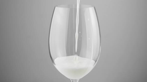 A glass into which white milk is poured on a gray background. Milk in a glass close-up. alt