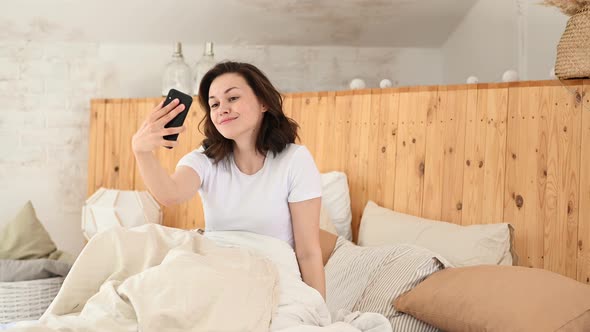 a Young Girl is Lying in Bed and Takes a Selfie and Sends a Photos