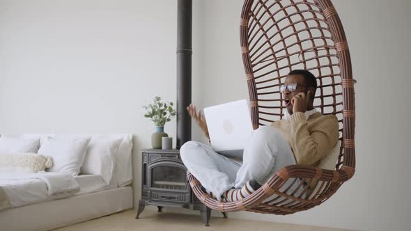 Black Freelancer Talks on Phone Swinging in Basket Armchair alt