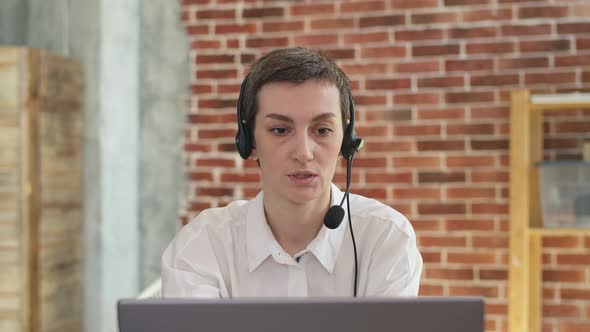 Operator woman in headset and white shirt talking while working behind a laptop alt