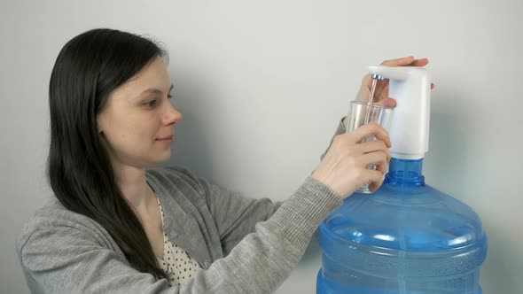 Woman is Pouring Water Into Glass From an Automatic Water Cooler and Drinking