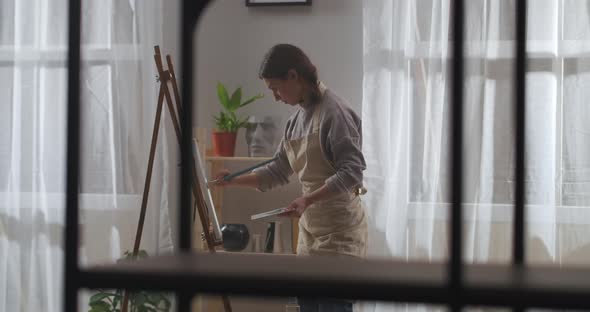 Home Studio of Young Female Painter Woman Is Drawing Picture on Canvas in Living Room of Apartment alt