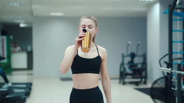Pretty woman in a black top is drinking a drink from a yellow shaker alt