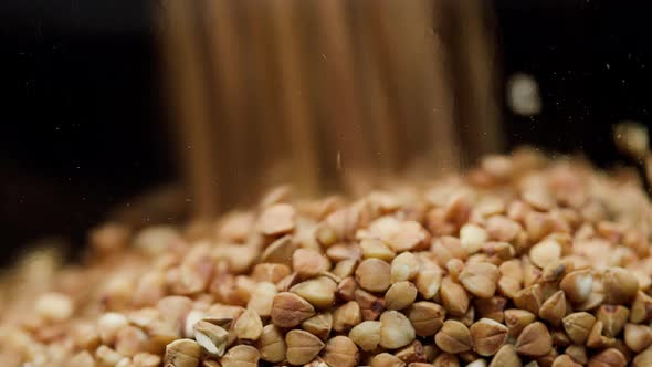 Closeup of Falling Down Buckwheat Into Glass Jar on Black Background alt