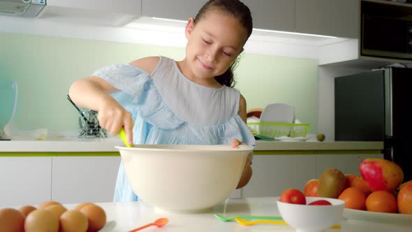 Happy Cute Eightyearold Girl is Cooking in the Kitchen Someone's Daughter is Whipping a Mixture with