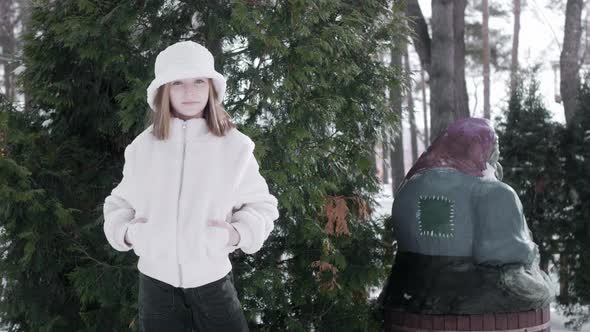 Cute Cheerful Girl Standing Near Green Thuja Plants and Dancing at Wintertime alt