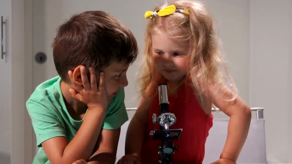 Little Boy in a Green Tshirt and a Cute Girl are Looking Through a Microscope alt