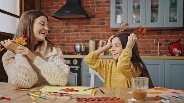 Young Mum and Little Daughter Laughing Fooling Around with Autumn Leaves While Drawing alt
