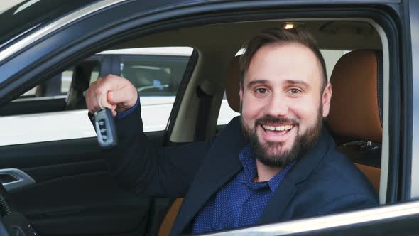 Man Sitting in His New Car Smiling To the Camera Showing Car Keys To His Newly Bought Vehicle
