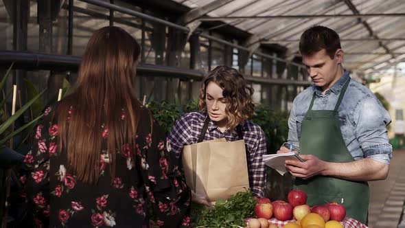 Cheerful Salescouple Wearing Apron are Selling Organic Food to Customer in Greenhouse alt
