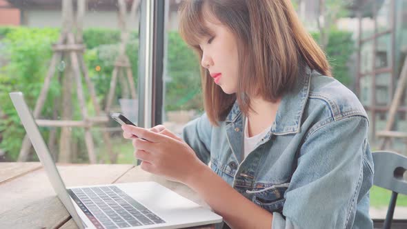 Asian woman working, doing projects on laptop and using smartphone while sitting on table