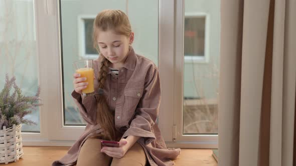 Girl Drinking Juice with a Phone in Her Hands