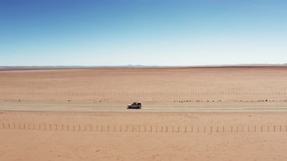 SUV White Automobile Vehicle Driving On Gravel Road In A Sandy Landscape In Namibia - Drone Shot alt