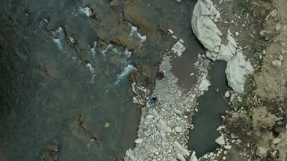 Couple Walking Rocky River Shore Looking Around Enjoying Warm Summer Cloudy Day alt