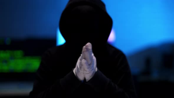 Silhouette of Unrecognizable Hacker in Black Hoodie Rubbing Hands in White Gloves alt