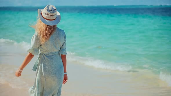 Girl Walking On Ocean Beach. Woman Relaxing On Bahamas Flowing Dress Blowing In Wind. Woman In Hat. alt