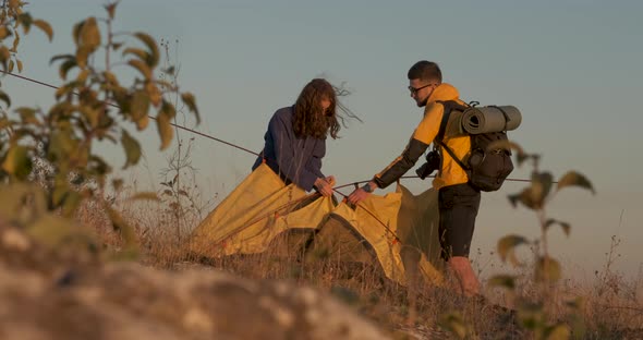 Two Young Travelers Make a Tent During Sunset to Spend the Night on Top of Hill