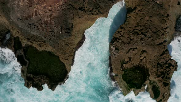 Top down aerial view of waves crashing into a small rocky bay