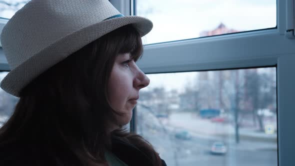 Brunette Woman in a Hat Looks Out the Window Drinks Soda and Smiles Autumn Weather Outside the