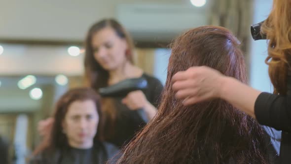 Woman Dries Brunette Hair with Hairdryer in Beauty Salon