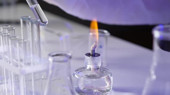 Close-up hand medical virologist holding test tube with biomaterial over fire alt