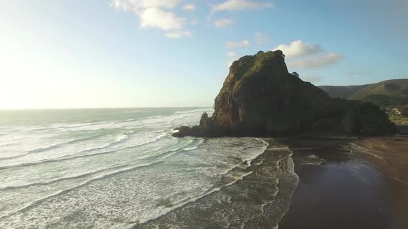 Aerial wide angle of Lion Rock Piha tracking towards as the waves gentle crash on the shore line, pa alt