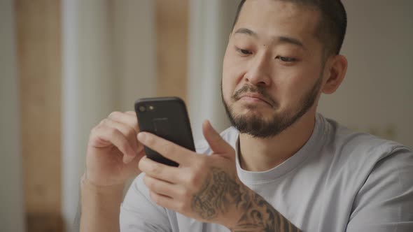 Young Adult Tattooed Asian Man is Surprised While Browsing on His Smart Phone alt