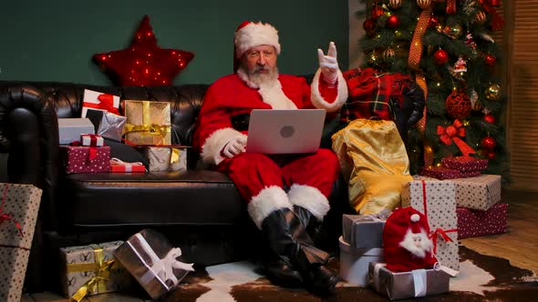 Cute Santa Claus Communicates By Video Call Using a Laptop alt