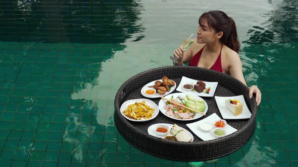 cheerful young woman enjoying with floating food and drinking champagne glass in swimming pool