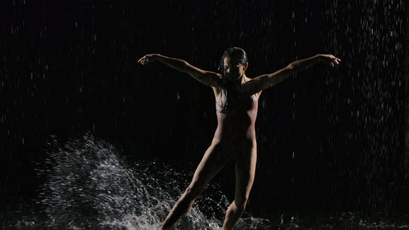 Wet Young Woman in a Tight Beige Swimsuit Is Dancing on the Floor Under the Rain and Splashes of alt