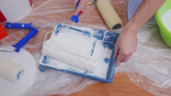 Closeup of Male Hands Drive a Paint Roller Over a Pallet with White Paint Picking Up Paint alt