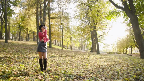 Stylish Girl Posing with Smile and Drinking a Cup of Tea in Sunny Autumn Park