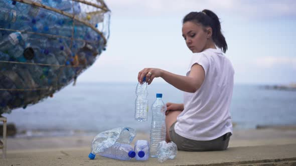 Back View of Young Tourist Sitting on Beach Leaving Plastic Bottles alt