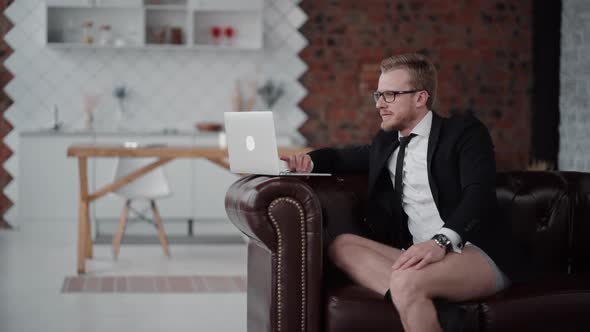 Young Successful Businessman Is Using Laptop While Sitting on Sofa in Apartment.