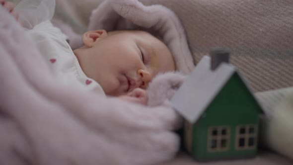 Closeup Portrait Cute Newborn Caucasian Girl Lying on Bed with Blurred Toy House alt