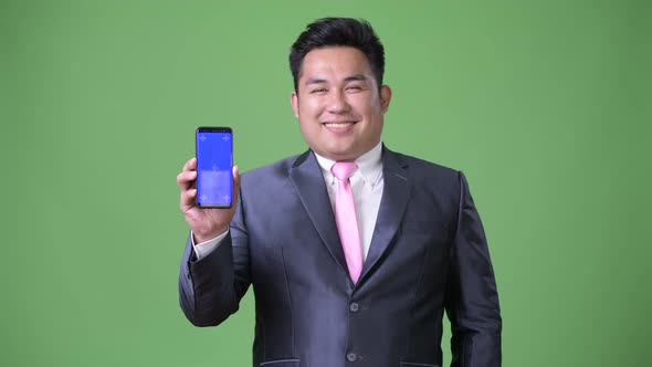 Young Handsome Overweight Asian Businessman Against Green Background alt