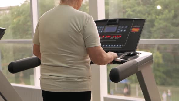 Eldest Woman of Retirement Age Runs on a Treadmill in the Gym