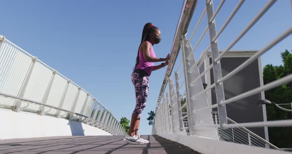 African american woman stretching her leg holding the railing of the city bridge alt
