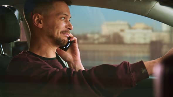 Attractive short-haired man drives a car and speaks on a smartphone.