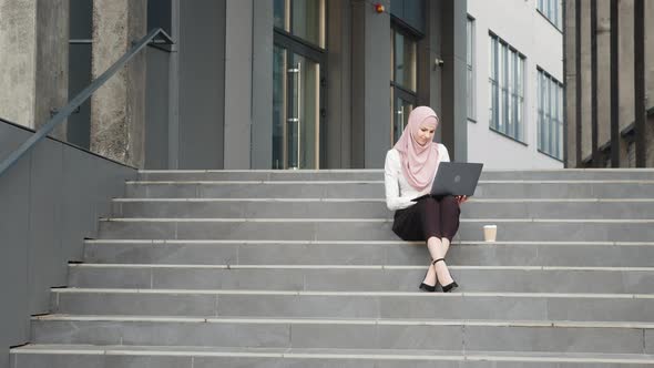 Young Muslim Woman Sitting on Stairs Near Business Center and Working on alt