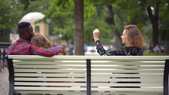 Cheating Boyfriend Hugging Girlfriend Holding Hands With Her Girl Friend Sitting On Bench In Park alt