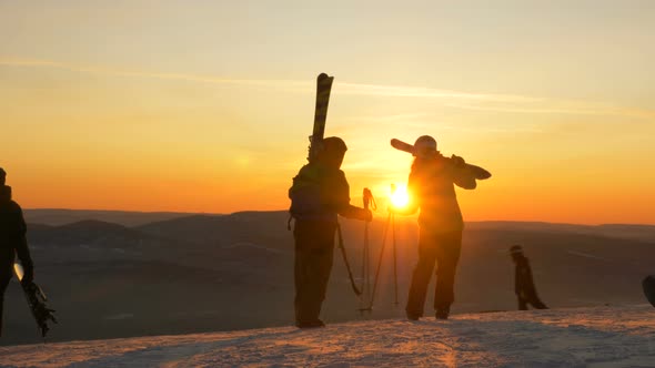 Skiers with Equipment Stand on High Hilltop Admiring Sunset alt