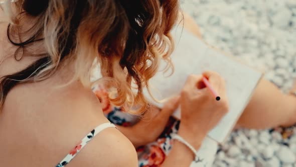 Close up view of a woman writing in her diary at sunset sitting on beach