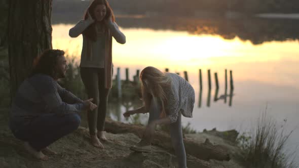 Young woman tying her shoelace and talking with friends on riverbank