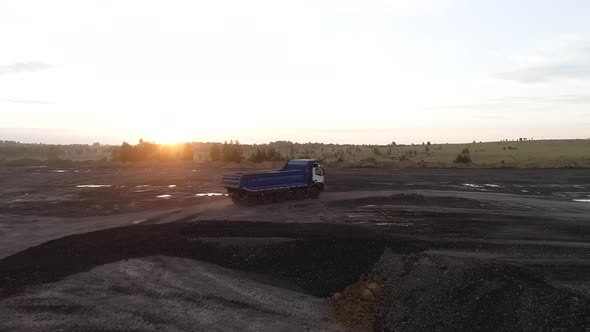 A Powerful Dump Truck is Driving Offroad in the Rays of the Setting Sun