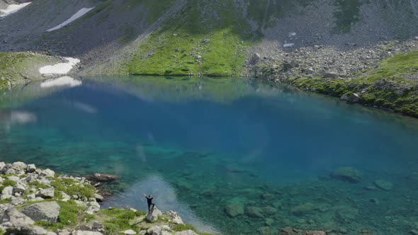 Aerial view of man traveler standing alone  hands up near emerald lake in mountains Arkhyz Russia alt