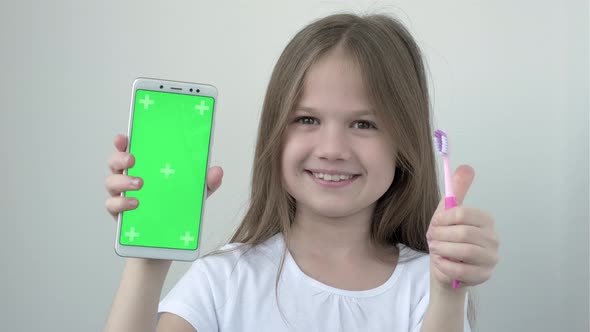 Little Girl in White Tshirt Shows Green Screen Phone and Toothbrush alt