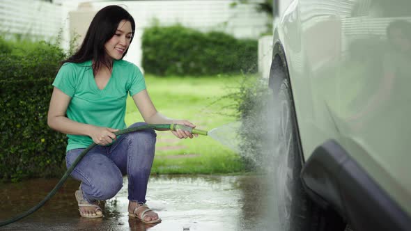 Young woman water spray her car wheel with water tube washing it