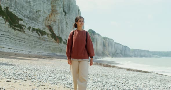 A Young Woman Walks Along a Pebbly Beach Past Sheer Chalk Cliffs