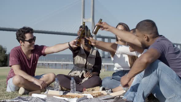 Relaxed Young People Clinking Beer Bottles in Park. alt